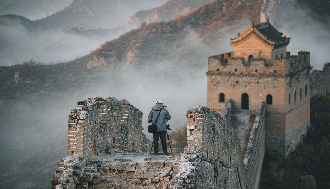 Dos viajeros con mochila en un tramo salvaje de la Gran Muralla entre la niebla al amanecer